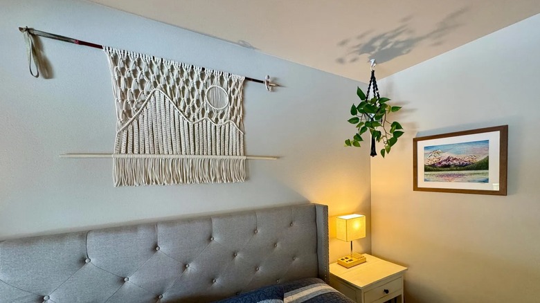 A ski pole holding wall art above a bed.