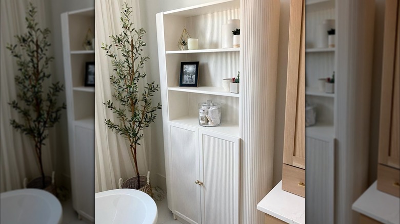 white billy bookcase holding bathroom decor next to bathtub and plant