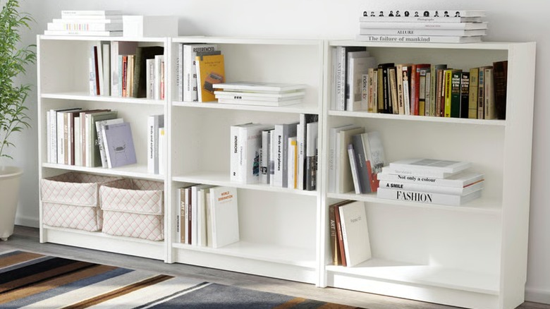 white bookcase filled with books and baskets next to plant