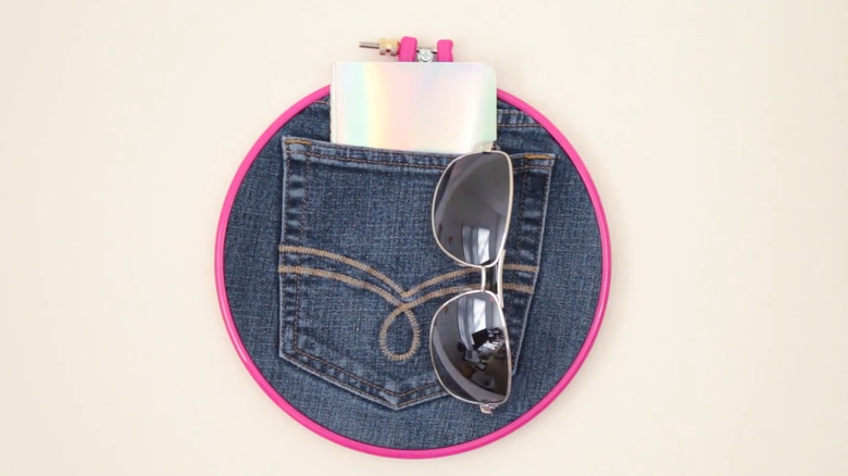 Pocket wall decor made from a denim pocket and embroidery hoop hanging on a wall with items in the pocket