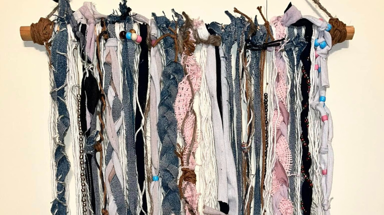 Close-up of a boho-style wall hanging made from strips of upcycled clothing on a wood piece