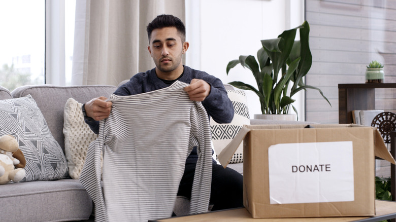 Man holding up a striped long-sleeved shirt while sitting on a couch with a 