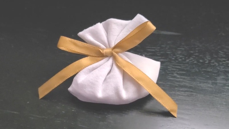 Scent sachet made from a section of tights tied with a gold ribbon sitting on a black table