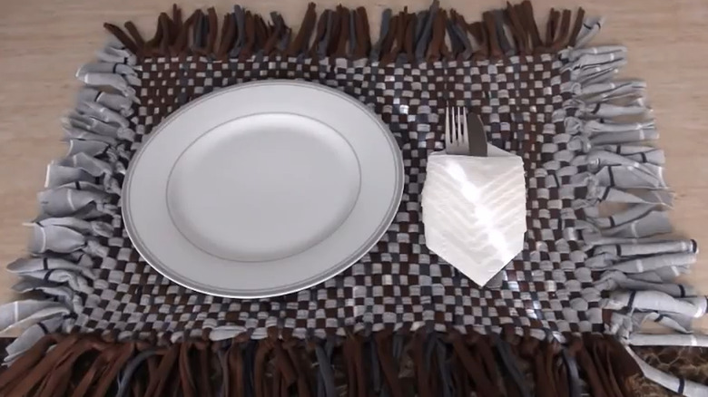 Gray and black woven placemat made from strips of clothing with a plate, napkin, and silverware on top