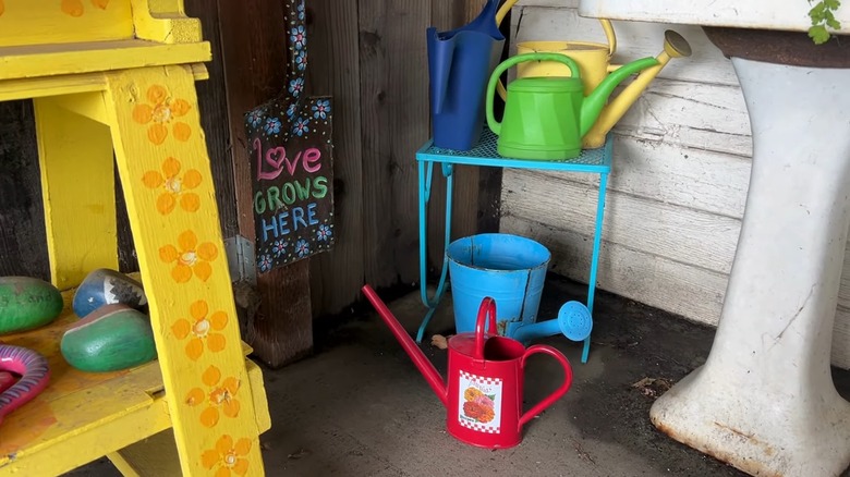 Colorful watering cans on a blue table near a decorated shovel