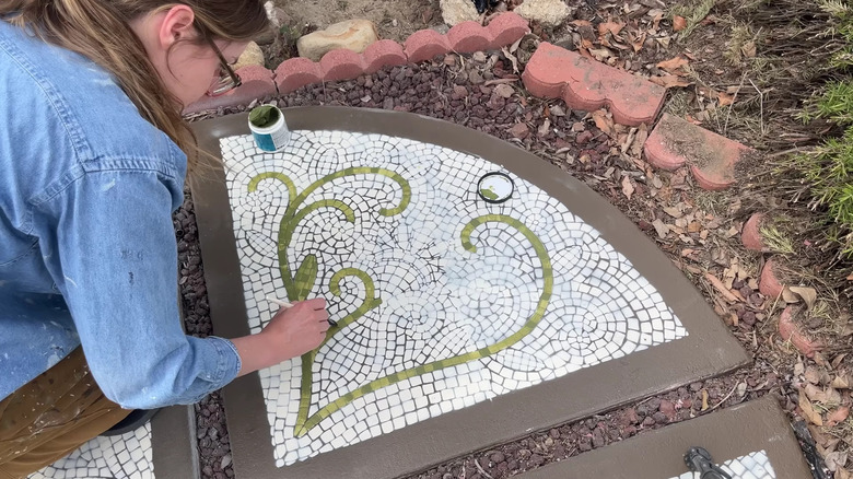 A person paints a mosaic pattern on stepping stones at the top of a driveway.