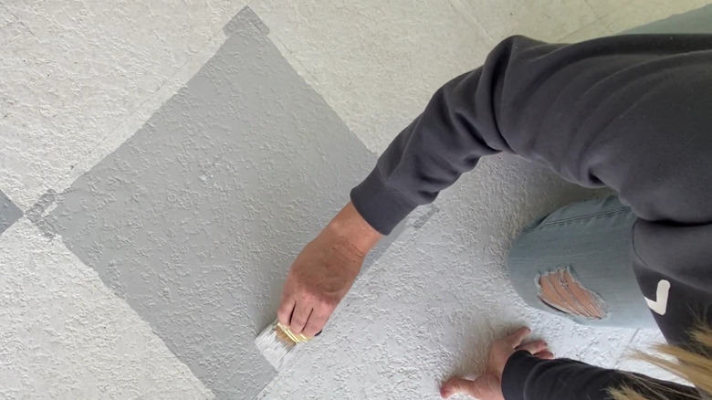 A person painting a checkerboard design on a driveway.