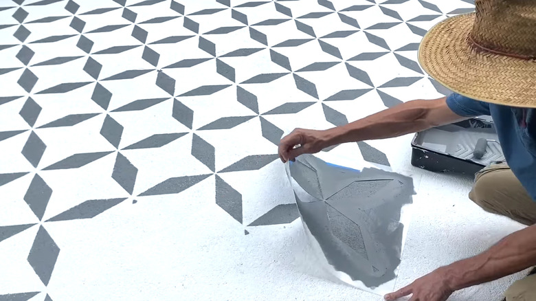 A person stencilling a white-painted driveway with encaustic tile patterns.