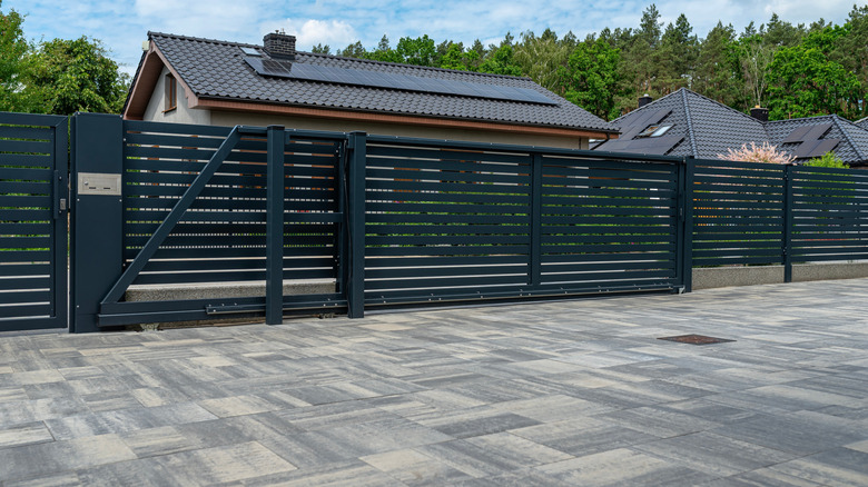 A paved driveway with pavers painted with an ombre effect in front of a fenced-in modern home.