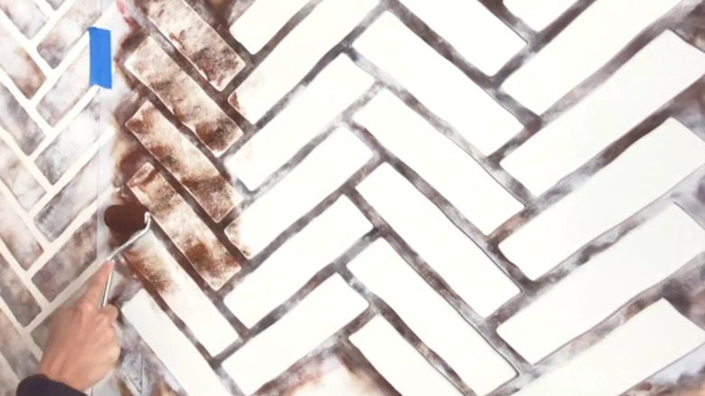 A person uses a small paint roller to add texture to a stencilled herringbone pattern.
