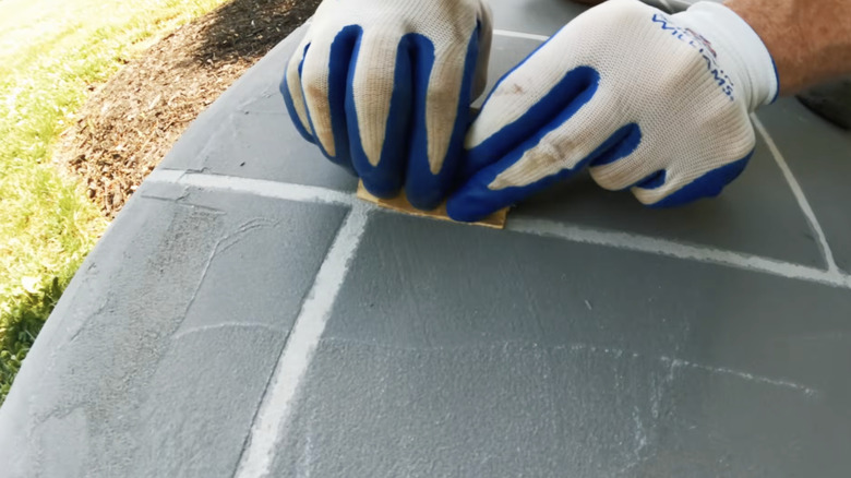 A person sands the grout lines on a driveway painted with faux porcelain tiles.