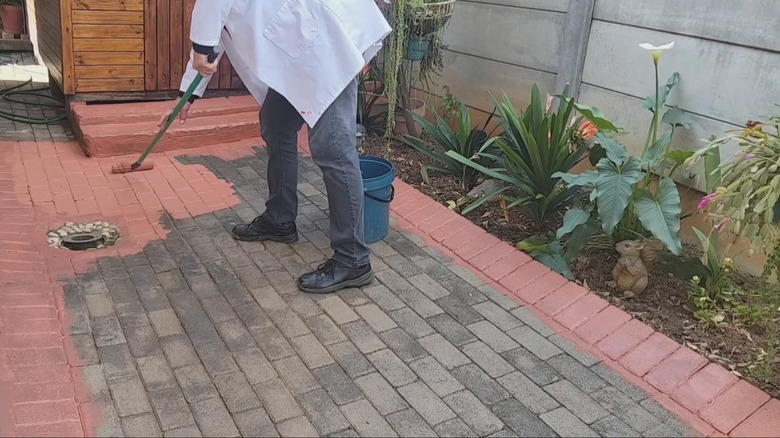 A person paints gray driveway pavers terra cotta with a roller.