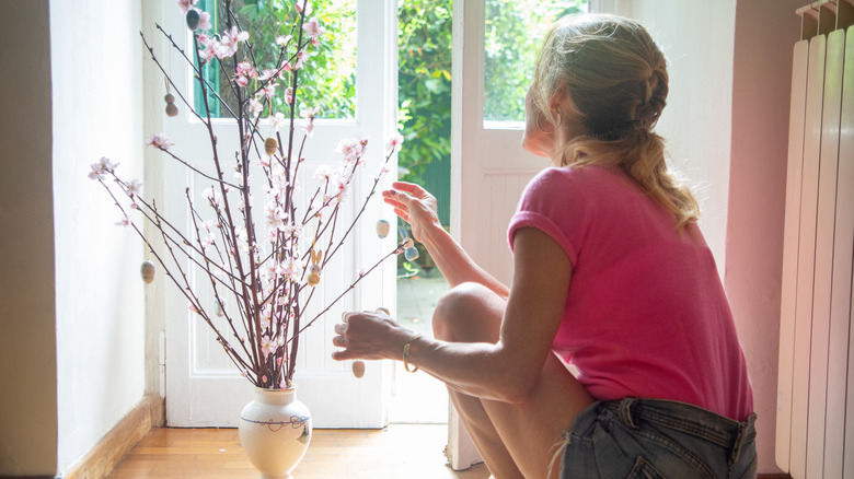 A woman squatting next to a growing peach tree with pink flowers
