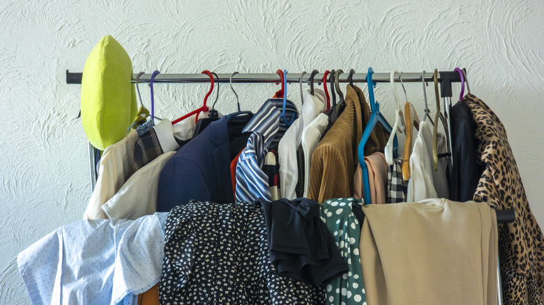 A lot of clothes hanging over a bar and hanging from a clothing rack