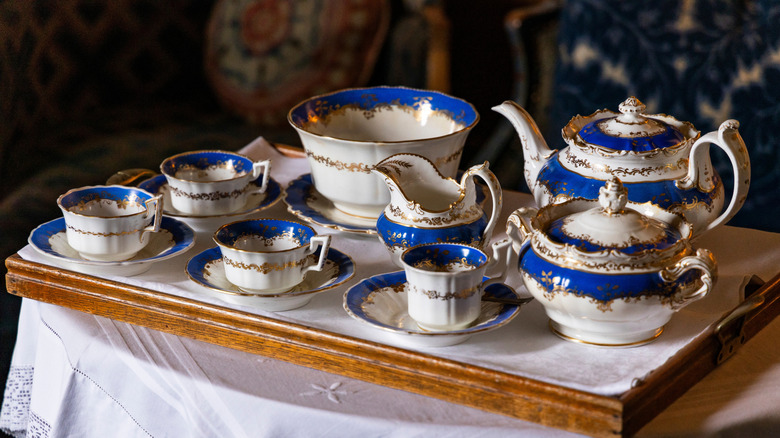 Fancy teapots and a tea set in white, blue, and gold and a serving tray on a white tablecloth