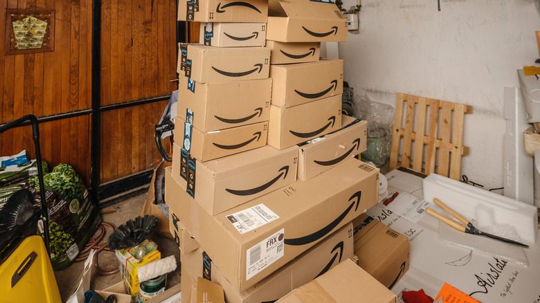 A large stack of Amazon boxes in a room with a bunch of other items including pallets. pruning shears, and bins around it