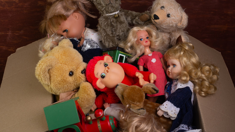 A cardboard box filled with old toys including dolls and stuffed animals