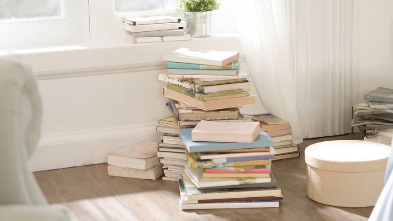 Many books precariously stacked in a living room by a window