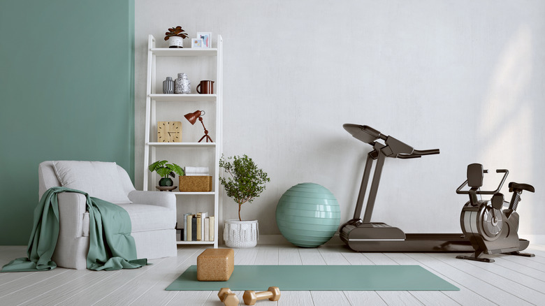 A home gym area next to a small chair and bookshelf with select items in teal