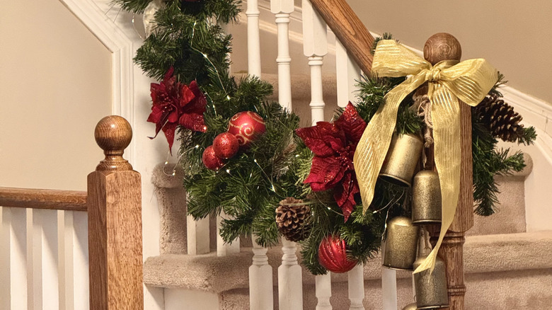 Pine garland on a stair railing with red accents, a gold bow, and antique bells