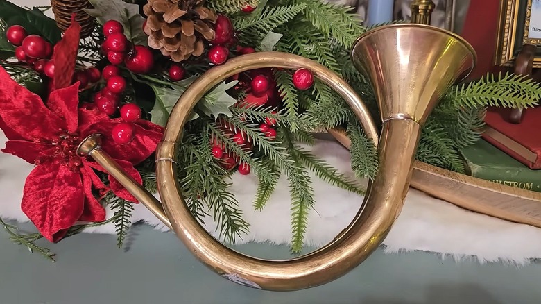 Old horn with an antiqued finish sitting next to Christmas florals