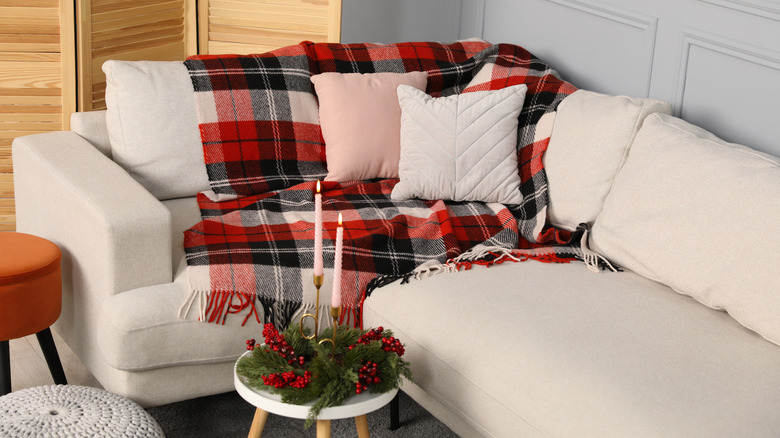 Cozy corner of a beige sectional with a green, red, and white plaid throw blanket and pillows