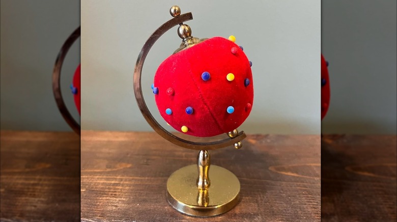 A red pin cushion on globe base next to ruler.