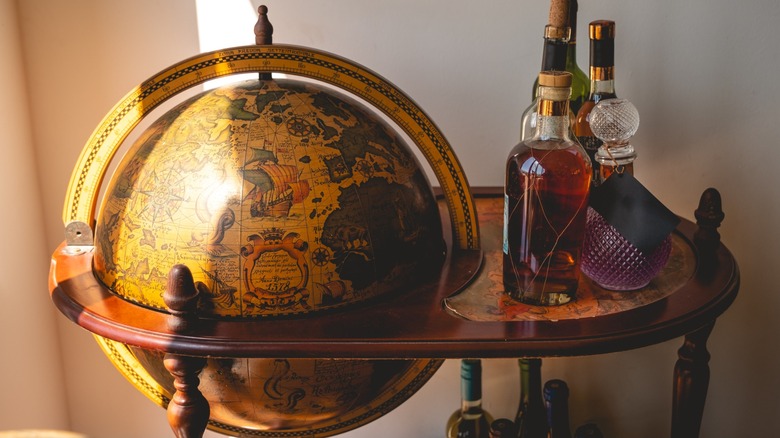 A vintage globe bar cart with alcohol on the stand
