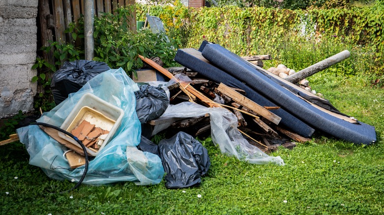 Pile of debris near a home in the yard, bags of trash and random materials cast on the lawn