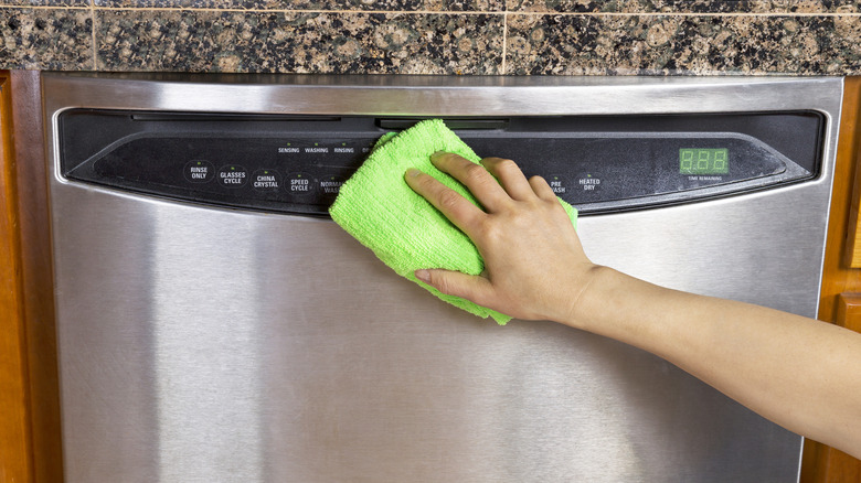Person wiping down the control panel of a dishwasher with a bright green cloth