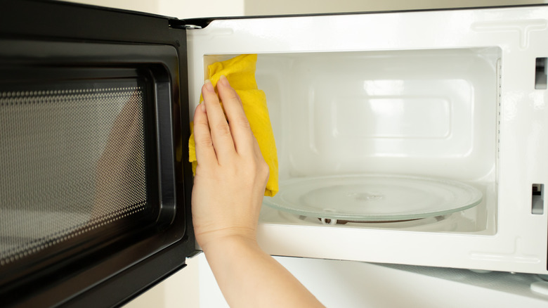 Person's hand wiping the inside of a microwave with a yellow cloth