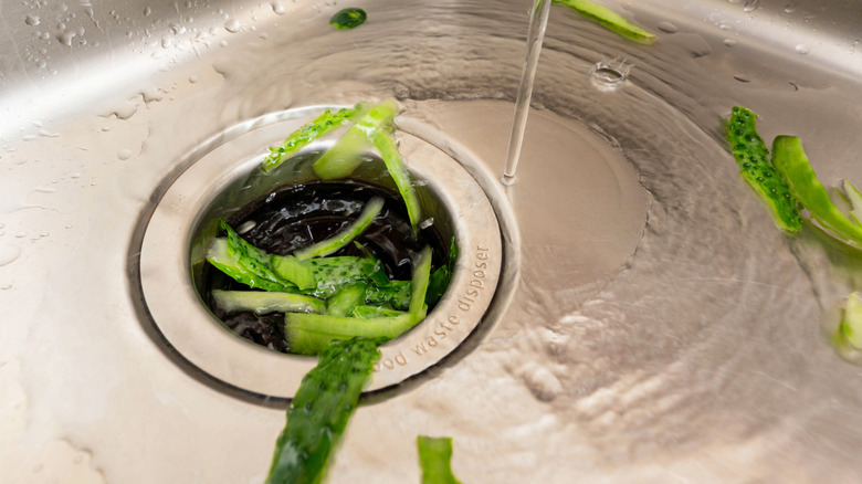 Vegetables being put down a kitchen sink garbage disposal with water running