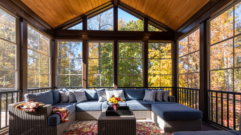 Contemporary three-season porch with wicker furniture in it and trees outside of the windows