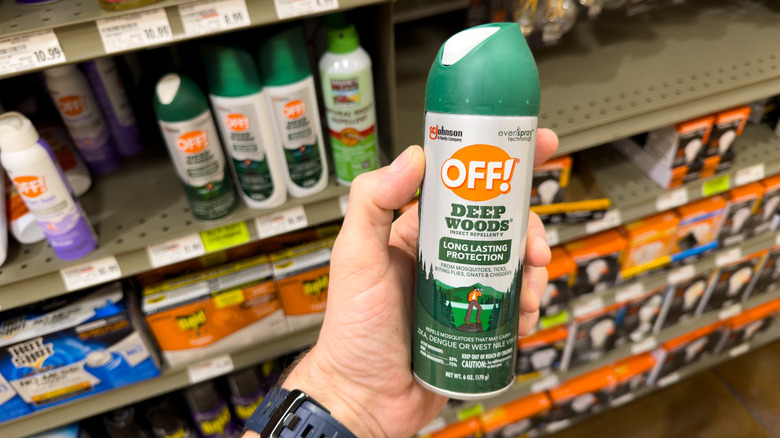 Person's hand holding a can of Off! insect repellent spray in front of a store shelf