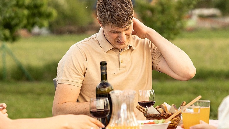Person having dinner outdoors touches their neck in reaction to a bug bite