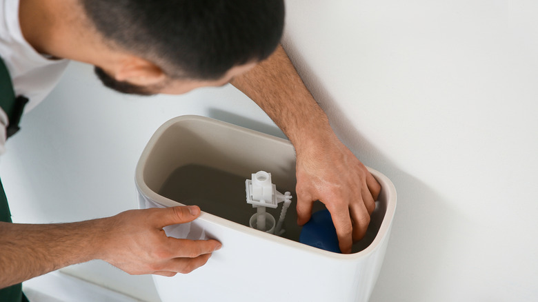 Male plumber replacing fill valve in toilet tank, closeup