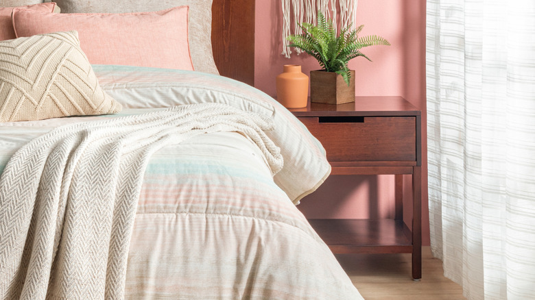 A bedroom with blush pink walls and a dark wood nightstand.
