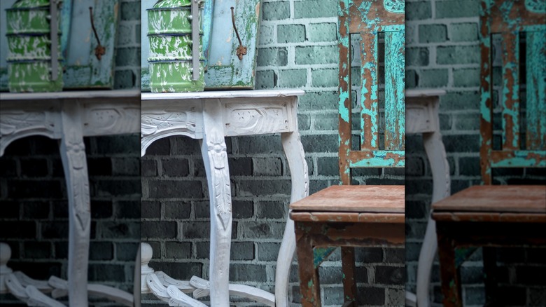 A vintage dark wood chair with peeling teal paint against a cerulean blue brick wall.
