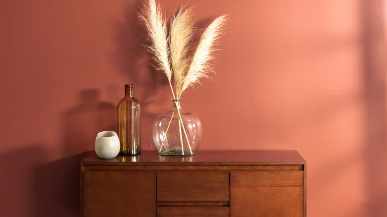Rustic-chic inspired vignette on a midcentury walnut sideboard against a terracotta-painted wall.