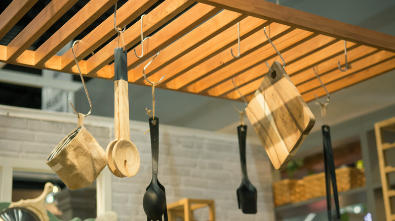 Cooking utensils hang from a pot rack mounted to the ceiling of a kitchen.