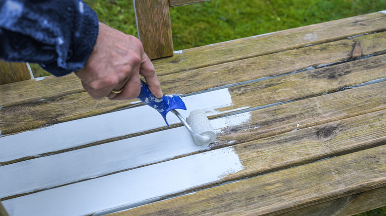 A crafter paints a garden bench made from old deck railings white.