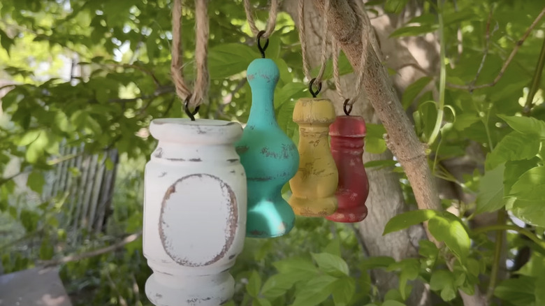Garden ornaments made from painted pieces of porch railing spindles hang from a tree branch in the backyard.