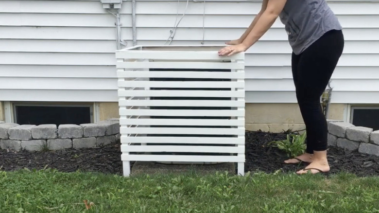 A woman repositions her an AC condenser unit cover constructed from repurposed porch railing.