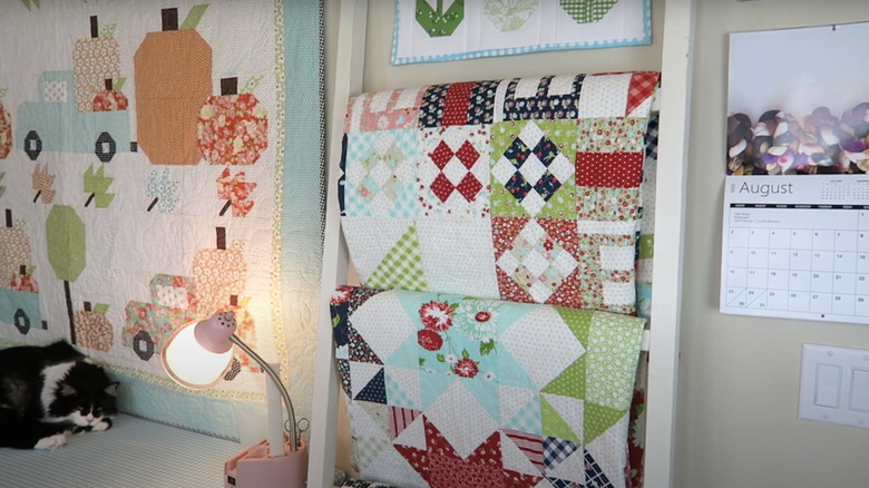 Homemade quilts hang neatly over a ladder made from porch railings and leaning against a wall.
