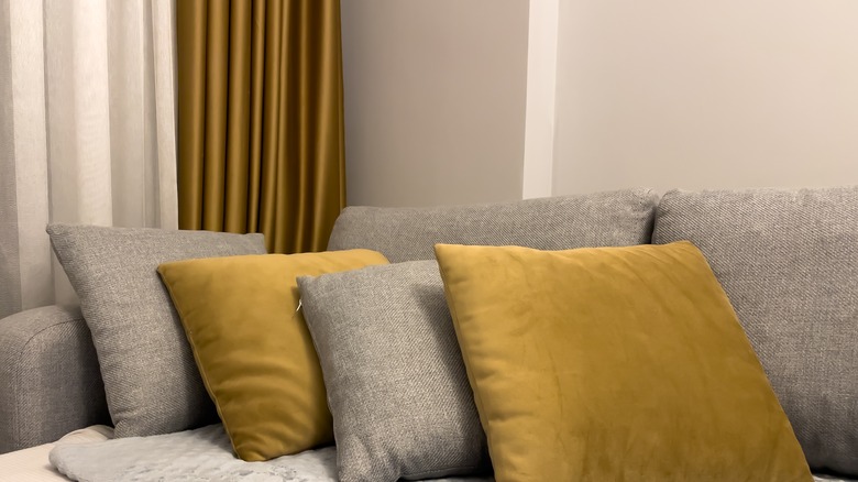 Mustard yellow drapes and a gray couch with mustard yellow throw pillows in a room with khaki-colored walls.