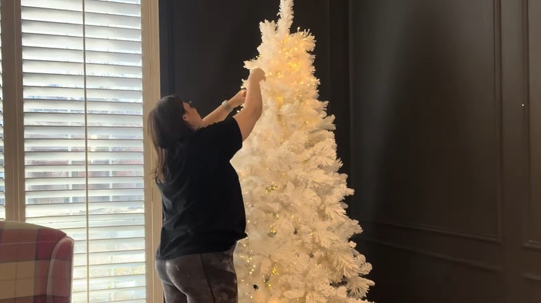 Woman putting string lights on a white Christmas tree in a zigzag pattern