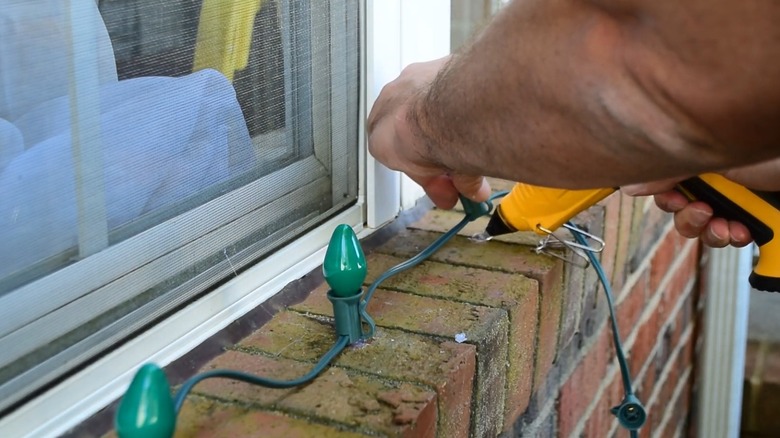 Hands applying hot glue under lights on brick exterior