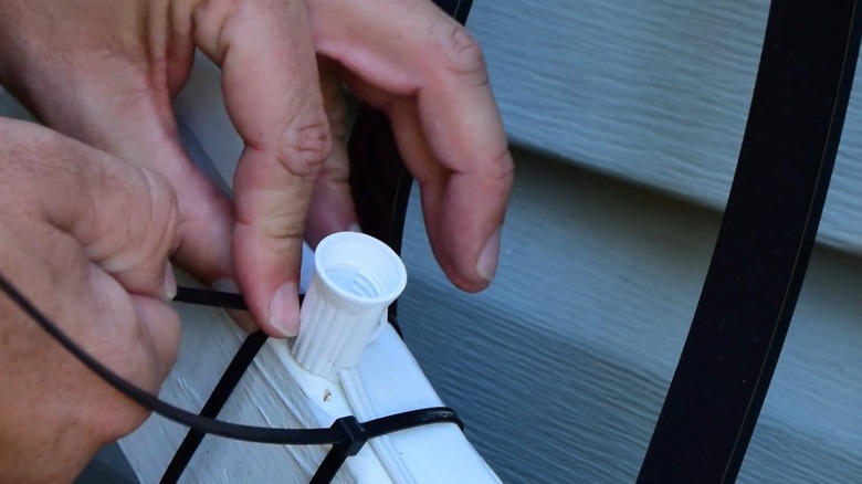 Hands tightening black zip ties around a white railing