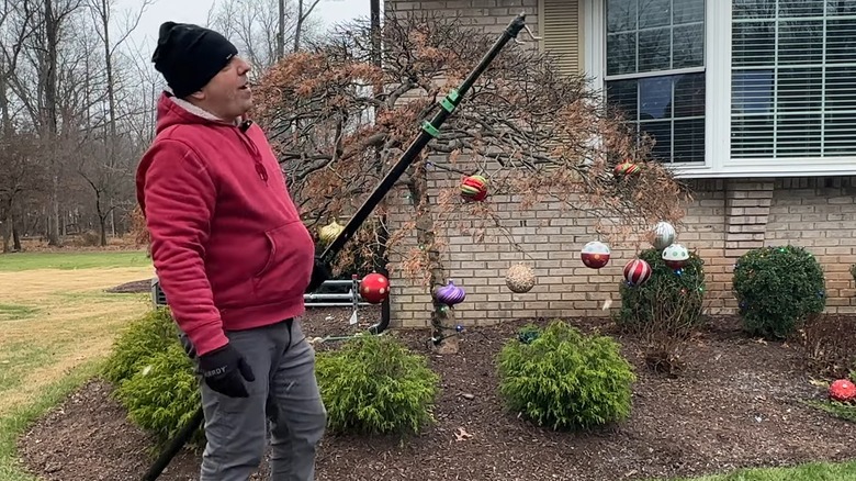 Man holding a black telescopic pole with hooks attached to its end