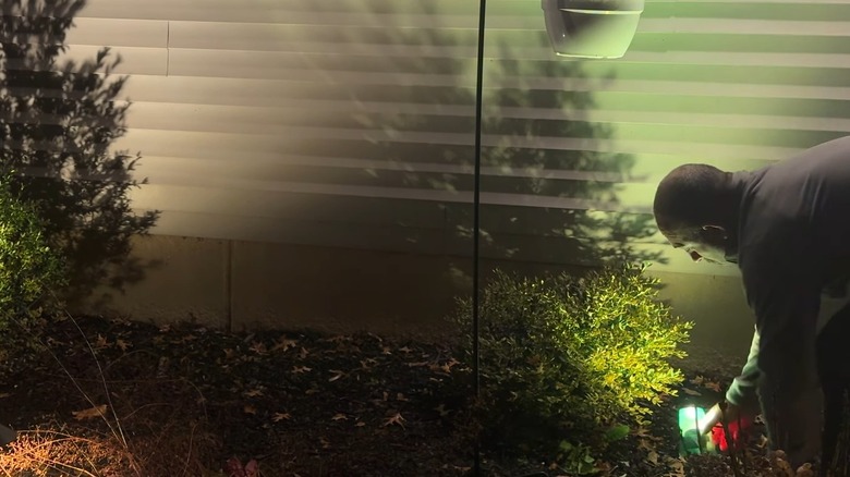 Man putting a green plastic cup over a yard light